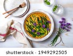 Small photo of Green asparagus, sweet peas Tart with edible chives flowers or blossoms. Seasonal spring dinner table, overhead view.