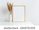Blank artwork frame mockup with stylish dry grass decoration in white vase, scandinavian room interior