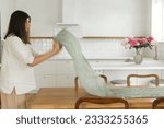 Woman arranging green textile table runner on wooden table in new modern home. Young female decorating dining room on background of minimal white kitchen, moving in and housekeeping