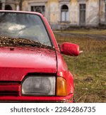 Small photo of An old, dilapidated, neglected red car. Red - once a great car - stands against the background of a destroyed historic building, the car is covered with leaves and twigs.