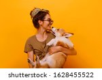 
Cute brunette woman in white t shirt and jeans holding and embracing Shiba Inu dog on plane red background. Love to the animals, pets concept. cheerful  woman holding Welsh Corgi puppy