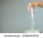 Small photo of making cookies. pouring flour from the hand into a bowl. flour particles fly from hand to bowl. close-up photo of a girl's hand pouring flour into a bowl. visible particles of flour