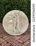 Small photo of Weathered garden roundel made from composition stone. The roundel depicts a pair of trumpeters in a classical scene.