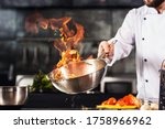 Chef hands keep wok with fire. Closeup chef hands cook food with fire. Chef man burn food at professional kitchen.