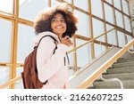 Smiling girl looking back while standing on stairs in school. Student going for the lecture.