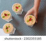 Small photo of Hand holding delicious trifle or tipsy pudding in glass topped with cherry. top view