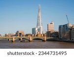 Shard tower amidst buildings with clear sky in background. Downtown district in city of London. Southwark bridge over river Thames on sunny day.