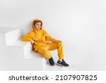 a teenager in a yellow tracksuit on a monochrome background in a hood is sitting on the steps