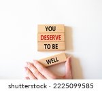 Small photo of You deserve to be well symbol. Wooden blocks with words You deserve to be well. Beautiful white background. Businessman hand. You deserve to be well concept. Copy space.
