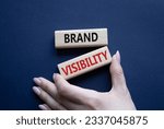 Small photo of Brand visibility symbol. Wooden blocks with words Brand visibility. Beautiful deep blue background. Businessman hand. Business and Brand visibility concept. Copy space. Conceptual word
