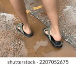 Small photo of The feet of a girl walking on the croon water on the road. walking on a muddy road.