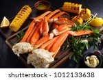 snow Crab legs served with melted butter, garlic cloves, lemon slices, grilled corn in cobs and fresh parsley on wooden cutting boards, horizontal view from above, close-up
