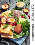 Small photo of ploughman's lunch of toasts, cheddar cheese, apple, scotch eggs, sliced head cheese, tomatoes, spinach, hot mustard, pickled onion on a white plate on an old wooden table, vertical view