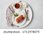 Morning breakfast: czech trdelnik or trdlo filled with cream decorated with mint, served on a white dessert plate, with cutlery, a cup of espresso coffee with milk on a serving tray, top view