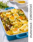 Small photo of Welsh Anglesey Eggs, soft mashed potatoes with hard-boiled eggs all smothered in thick creamy leek and cheese sauce in baking dish on white table, vertical view, close-up