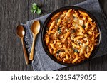 Ground Chicken Pasta Bake with onion, mushrooms, spinach, tomato sauce and mozzarella cheese in baking dish on dark wood table with spoons, horizontal view from above, flat lay, free space