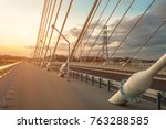 sidewalk and highway going through a cable-stayed bridge with big steel cables, closeup at evening time during a sunset against a background of sky, clouds and sun rays