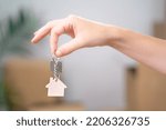 Female Hand Holding House Keys Inside Empty Room with Boxes Banner. Real estate agent handing over house keys in hand. Close-up view of keys from new home on cardboard box during relocation.