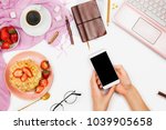 Beautiful flatlay arrangement with cup of coffee, hot waffles with cream and strawberries, laptop and woman hand's holding smartphone: concept of busy morning breakfast, white background.