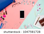 Frame flatlay with woman's blue purse, glasses, smartphone with black copyspace, cosmetics and stationary supples. Pastel pink and mint background, business mockup, women work bag contents