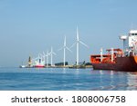 A seaport on the outskirts of Amsterdam with wind generators on the coast and solar panels mounted on mooring posts.