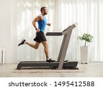 Full length profile shot of a young man running on a treadmill at home 
