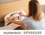 Small photo of Young mother putting compress on forehead to bring down temperature of sick daughter with fever lying under blanket at home. Parent caring for sick child lying in bed with flu. Concept of unwell child