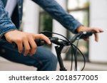 Close-up hands of unrecognizable cyclist male pressing handlebars on handlebars of bicycle outdoors on blurred background. Side clsoep view of bicyclist checking work of braking system of bike.