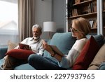 Small photo of Simple living. Happy middle-aged senior couple 70s husband and wife sit relax on couch in living room reading book drinking tea together, calm elderly 60s couple booklovers rest at home enjoy life