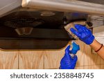Woman's hands cleaning or servicing kitchen chimney wearing rubber gloves and using cleaning liquid..