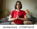Self awareness and mindfulness concept. Attractive young woman having premature graying meditating at home with eyes closed, focusing on breathing, feeling present moment, making namaste gesture