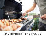 Hand of young man grilling some meat and vegetable-meat skewers on huge gas grill (Shallow DOF)