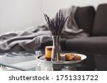 Living room decor: glass coffee table with dried lavender bouquet and aroma candles on a metal tray, sofa and blanket on background. Scandinavian style. Simple home decoration