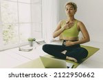 Small photo of African female yoga teacher having online lesson sitting on green mat in light room showing pranayama techniques, hands on her chest and belly, looking concentrated and focused on body feelings
