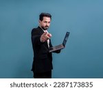 Small photo of Successful businessman in black suit with innovative tech concept, finger pointing at camera and holding laptop and smiling with excitement on copyspace background for promotion or ad. Fervent