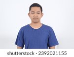Small photo of Close up of Asian man with blue navy casual t-shirt emotionless face, looking at camera isolated over white background wall.