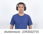 Small photo of Close up of Asian man with blue navy casual t-shirt emotionless face, looking at camera using earphone isolated over white background wall.