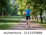 Young man running in park with headphones on sunny summer day