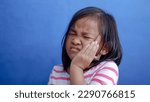 Small photo of Asian kid girl toothache. Kid suffering from toothache. Asian child hand on cheek face as suffering from facial pain, mumps toothache. Dental health care.