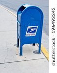A blue US post office box on sidewalk corner.