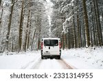 Camper Van driving on a road through a snow covered forest in winter, adventure vacation and lifestyle in the woodlands, Germany 