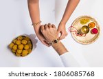 Close up top view of female hands tying colorful rakhi on her brother’s hand isolated on white background on Raksha Bandhan Festival