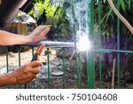Small photo of Technician industrial worker welding repair fence metal steel. Flash burn, ultraviolet light, sparks, infrared light effect, technician use welding mask to protect the eyes. Industry concept.