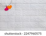 Small photo of Engagement valentines day. Two hearts on rope are connected by one clothespin on white brick wall background. Romantic marriage proposal and wedding. Symbol and concept of marital fidelity. Copy space