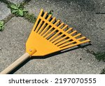 Small photo of Plastic garden rake with wood handle for clearing dried leaves, lying on backyard stone slabs unused