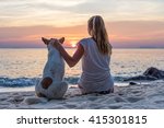 Young woman with dog sitting on the beach and watching the sunset
