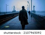 Back of cinematic young man in winter coat walking outside in urban city on bridge on a moody, foggy, winters night.