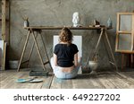 Woman painter sitting on the floor in front of an empty canvas and drawing. Art studio interior. Horizontal drawing background. Creative concept