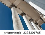 Gaze from below at neoclassical colonnade: tall white columns with floral capitals against blue sky, elegant slant, and grand ceiling view.