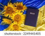 Bible (Holy Writ) and sunflowers on background of flag of Ukraine.